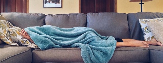 Person laying on couch under a blanket