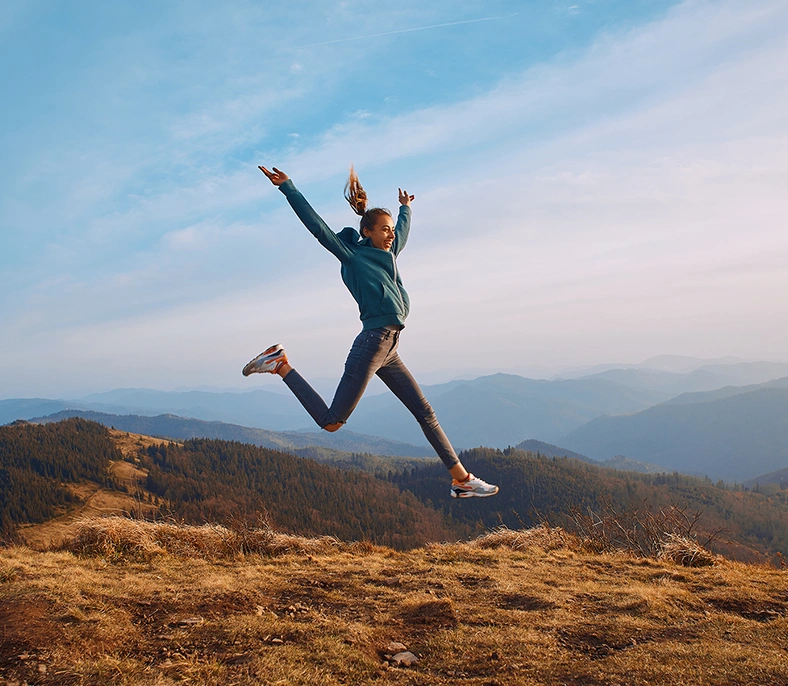 Exuberant woman on a hike, jumping with arms and legs outstretched