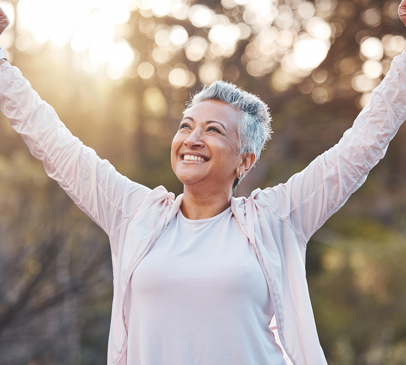 Femme âgée souriant les bras levés en plein air au coucher du soleil