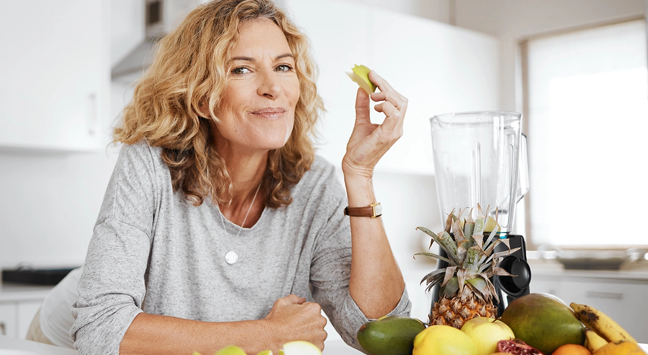 Smiling woman enjoying some fruit while making a smoothie