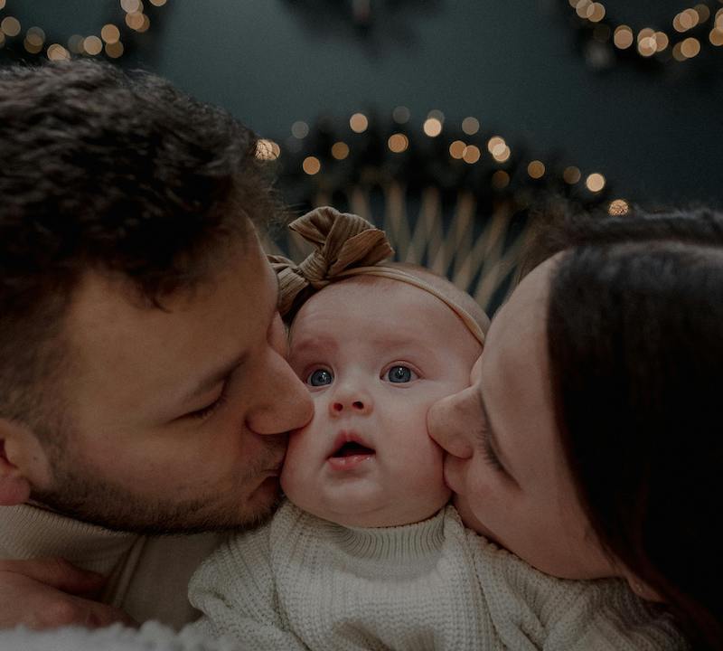 A mom and dad kiss their newborn baby on the cheek